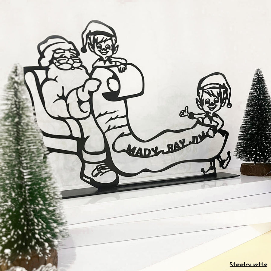 Steel decorative gift item featuring two elves showing Santa Clause who their favorite family is