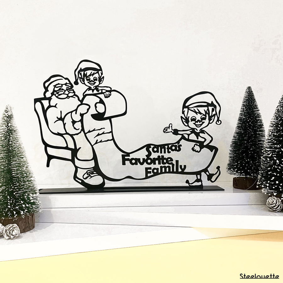 Steel decorative gift item featuring two elves showing Santa Clause who their favorite family is