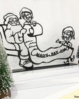 Steel decorative gift item featuring two elves showing Santa Clause who their favorite family is